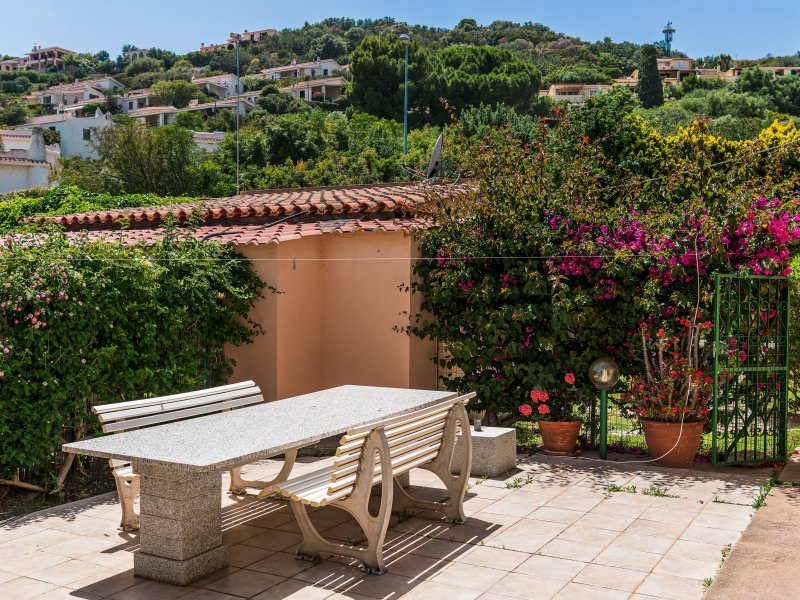 Großer, stabiler Granittisch inmitten blühenden, mediterranen Planzen mit Blick auf die Hügel von Costa Rei Großer, stabiler Granittisch inmitten blühenden, mediterranen Planzen mit Blick auf die Hügel von Costa Rei